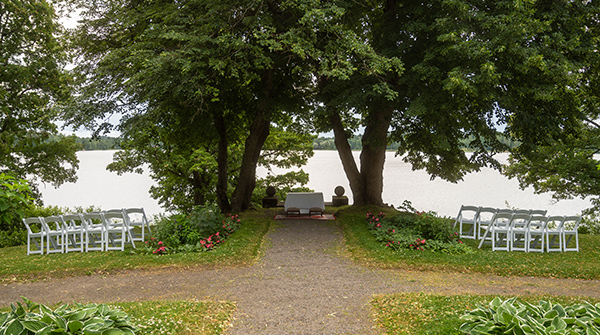 Vanajanlinnan puutarhassa puiden välissä vihkipöytä sekä nurmella tuoleja rivissä